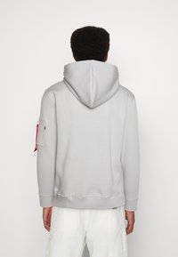 Sudadera con capucha de color gris claro, con un gráfico en la parte posterior, puños acanalados y un bolsillo con cremallera en la manga izquierda. Textura suave.