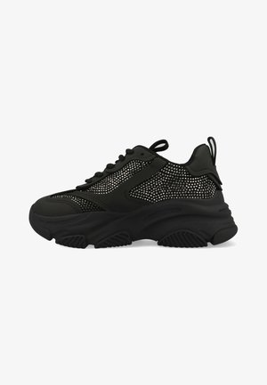 Black sneakers with a textured mesh panel, featuring a thick rubber sole, round toe, and laces. Small pull tab at the rear.