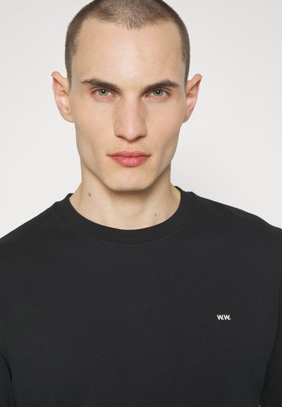Black cotton sweatshirt with a crew neck, featuring a small white logo on the left chest. Smooth texture and minimal design.