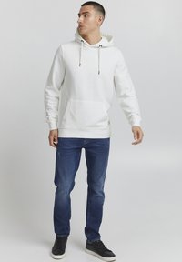 Witte hoodie met een kangoeroezak, gecombineerd met blauwe spijkerbroek en zwarte sneakers. Soepele textuur, casual pasvorm, minimalistisch ontwerp.