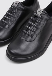 Zapatos de cuero negro tipo slip-on con cordones elásticos de rayas grises y negras y costuras decorativas alrededor de la punta y los laterales.