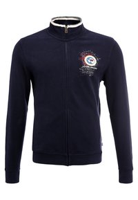Chaqueta azul marino con cremallera, fabricada en un tejido suave, que presenta un alto cuello, un acento blanco en el cuello y un gráfico estampado en el lado izquierdo del pecho.