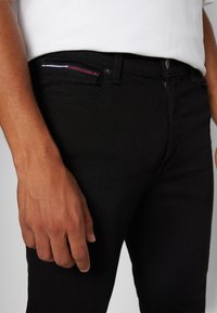Vaqueros de denim negro con un ajuste slim, que cuentan con un bolsillo para monedas en la parte delantera y un sutil detalle de costura en rojo, blanco y azul en el bolsillo.