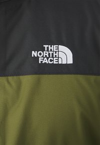 Sort og olivengrøn stof med et broderet hvidt logo, "THE NORTH FACE," der har et buet design i den øverste venstre del.
