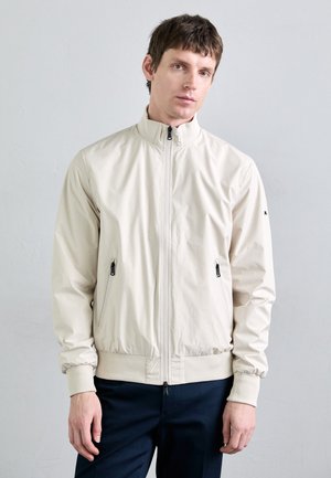 Ljusbeige zip-up jacka med hög krage, elastiska manschetter och två blixtlåsfickor på sidorna. Slät, matt yta med en figurnära design.