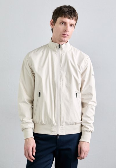 Hellbeige Zip-up-Jacke mit hohem Kragen, elastischen Bündchen und zwei seitlichen Reißverschlusstaschen. Glatte, matte Oberfläche mit tailliertem Design.