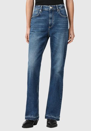 Femme portant un jean bleu taille haute à jambes droites avec une légère décoloration, associé à des bottes à talons noires et un haut noir.