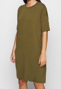 Oliwkowa sukienka t-shirtowa z miękkiego, lekkiego materiału. Posiada okrągły dekolt i krótkie rękawy, wyróżnia się luźnym krojem oraz bocznymi rozcięciami.
