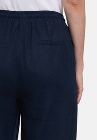 Pantaloni blu navy realizzati in tessuto testurizzato, con vita elastica e due tasche posteriori. Il design è semplice e funzionale.