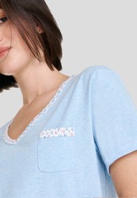 Camisa de manga corta azul claro con un cuello y bolsillo en el pecho de patrón floral. Tejido suave con un corte relajado y un diseño sencillo.