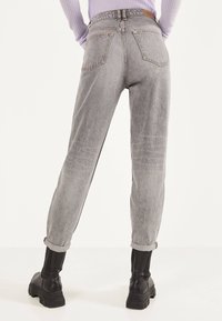 Jeans grises de talle alto en un ajuste tapered con los puños enrollados, con dos bolsillos traseros y costuras en contraste. Combinados con botas negras.