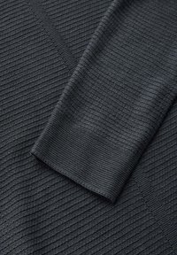 Gros plan sur un tissu noir tricoté avec une texture côtelée fine, montrant le détail d'une manche pliée.