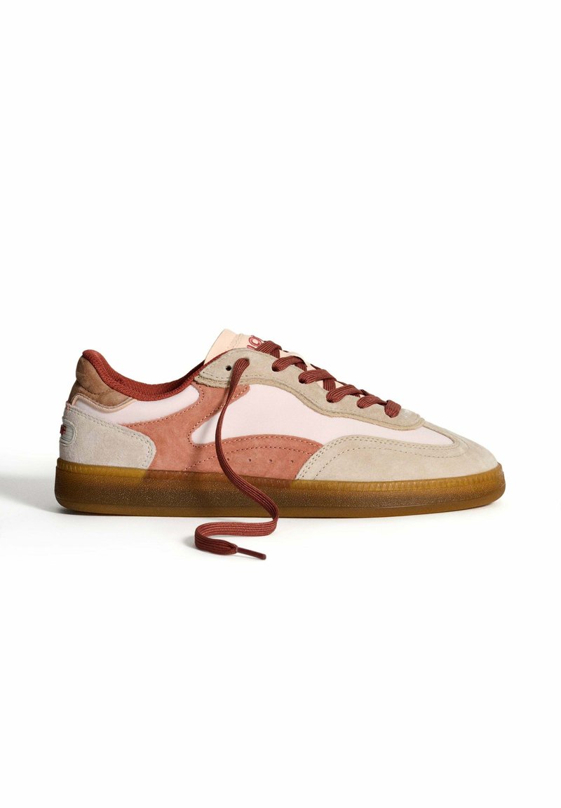 Zapatillas de ante en tonos beige, rosa y marrón. Cuentan con una suela de goma, puntera redonda y cordones marrones con un diseño en bucle en el lateral.