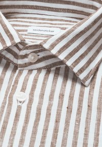 Chemise blanche et marron à rayures verticales avec un col pointu et deux boutons blancs visibles, avec une étiquette "seidensticker" à l'intérieur du col.