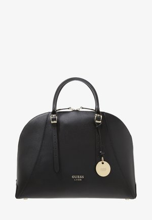 Sac à main en cuir noir de forme arrondie avec deux anses supérieures, boucles dorées, un étiquette ronde en or avec logo et un marquage "GUESS LUXE" sur le devant.