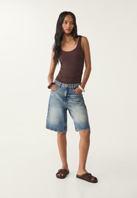 Brown fitted tank top, blue denim shorts with a relaxed fit and faded wash, dark brown slide sandals with studded accents.