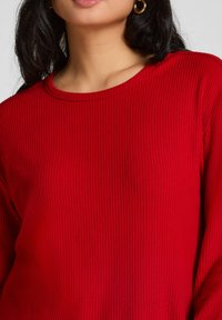 Rode geribbelde trui met lange mouwen en een ronde halslijn, met textuurstof en een nauwsluitend ontwerp. Geen zichtbare hardware of patronen.