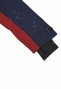 Tessuto sintetico idrorepellente in navy, rosso e nero con gocce d'acqua visibili sulla superficie; texture liscia; dettaglio di chiusura ai polsini.