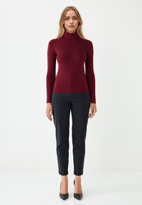 Burgundy turtleneck sweater in a fitted design, paired with black, slim-fit pants and black high heels. Smooth texture and solid color.