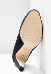 Mörkblå mockaskor med hög klack, spetsig tå, glittriga detaljer och en strukturerad gummisula. Varumärket "Gabor" och "Tillverkad i Portugal" är markerat.