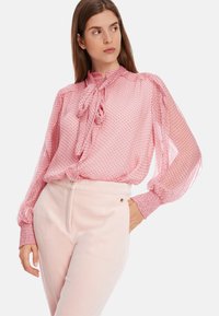 D blouse mit rosa Punkten, einem hohen Kragen, einer Schleifen-Detail und voluminösen Ärmeln, kombiniert mit hellrosa Cordhosen.
