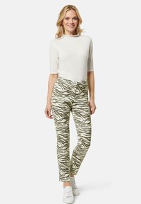 Witte t-shirt met korte mouwen, gecombineerd met gestreepte groen en beige tapered broeken met een tijgerstrepenpatroon, gedragen met witte sneakers.