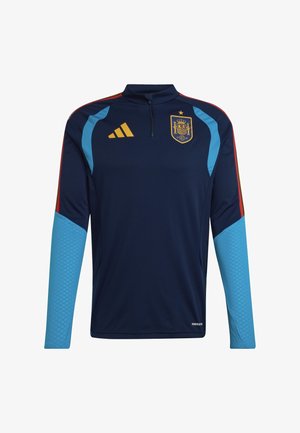 Tmavě modrý sportovní top s dlouhým rukávem, světle modré manžety na rukávech, červené a žluté pruhy na ramenou, žluté logo Adidas a emblém španělského fotbalového týmu na hrudi.