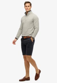 Lys grå halvdækkende pullover, marineblå shorts, brun læderbælte og slip-on loafers; glat tekstur, casual pasform og skræddersyet design.
