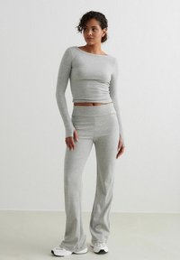 Maglietta grigia a maniche lunghe e pantaloni a vita alta coordinati, realizzati in un tessuto morbido con un design aderente, caratterizzati da cuciture sottili e maniche allungate.