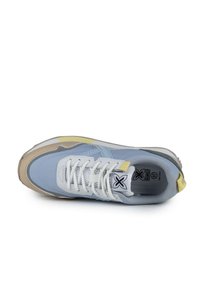 Zapatilla deportiva de color azul claro con una superficie texturizada, cordones blancos, acentos amarillos y una suela de goma beige. Presenta paneles de malla para mayor transpirabilidad.