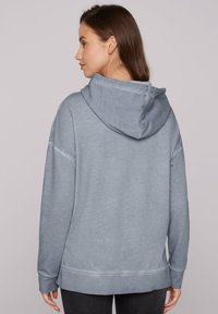 Felpa con cappuccio grigia, dal taglio rilassato, con una texture morbida e polsini a coste. Presenta una tasca a marsupio e una finitura leggermente lavata.