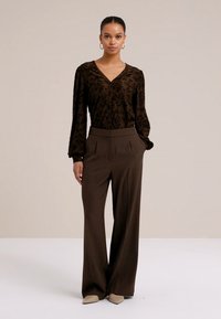 Pruun tekstuuriga pluus V-kaelusega ja nööpidega, mida on kombineeritud kõrge vöökohaga, laiade jalgadega pruuni püksiga ning beežide terava ninaga kingadega.