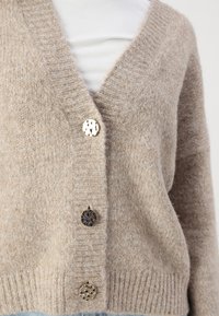 Beige gestrickte Cardigan mit V-Ausschnitt, drei dekorativen Knöpfen, gerippten Bündchen und weicher Textur. Hergestellt aus einem warmen, gemütlichen Material.