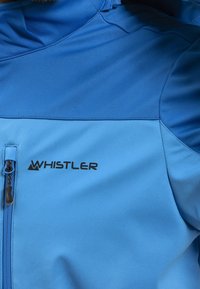Modrá bunda s měkkým pláštěm a kapsou na zip, s černým logem „WHISTLER“ a hladkou texturou. Horní část má kontrastní odstín.