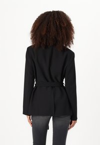 Črn poslovni blazer z zategnjeno pasom, dolgimi rokavi in peplum obliko. Gladek material z minimalnimi šivi.