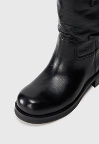 Bottine en cuir noir avec un bout arrondi, texture lisse, petit talon carré et coutures discrètes le long des seams.