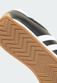 Baskets Adidas noir et blanc montrant la semelle en gomme avec un motif en zigzag et le logo Adidas embossé.