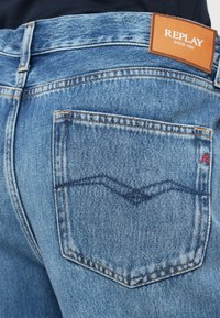 Μπλε τζιν παντελόνι μεDistinct ραφές, με ετικέτα σε πατζάκι στη μέση και μία πίσω τσέπη με καμπύλο σχέδιο.