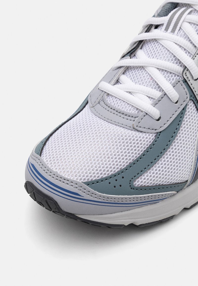 Chaussure de sport avec une tige en mesh blanc, des accents synthétiques gris et des rayures bleues. Comprend des lacets, des trous de ventilation et une semelle en caoutchouc texturée.