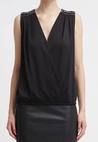 Hihaton musta V-kaula-aukkotoppi, jossa on koristeelliset helmirivit olkapäillä, yhdistetty mustaan nahkahameeseen.