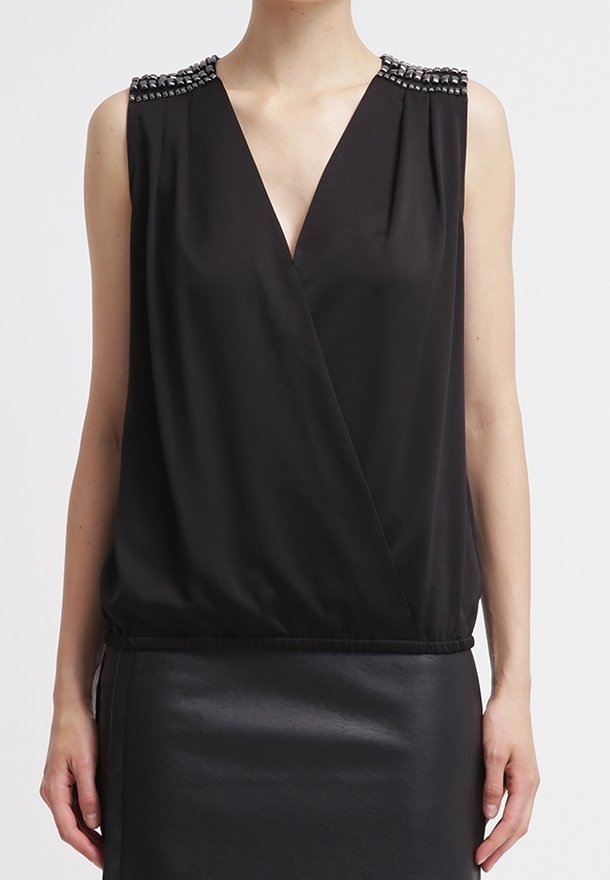 Hihaton musta V-kaula-aukkotoppi, jossa on koristeelliset helmirivit olkapäillä, yhdistetty mustaan nahkahameeseen.