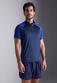 Ναυτικό μπλε κοντομάνικο αθλητικό μπλουζάκι με μισό φερμουάρ μπροστά, με αντίθετες μπλε λεπτομέρειες, κατασκευασμένο από μαλακό, ύφασμα που απορροφά την �υγρασία.