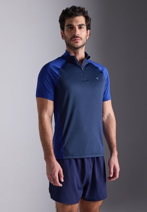 Camiseta atlética de manga curta azul marinho com fecho de meia-zíper à frente, apresentando detalhes em azul contrastante, feita de um tecido suave que absorve a humidade.