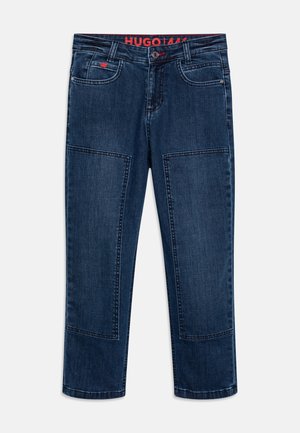 Vaqueros de mezclilla azul oscuro con corte recto, que cuentan con dos bolsillos delanteros, parches laterales y una pretina roja con marca. Detalle mínimo de costuras.