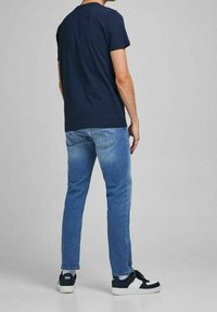 Mörkblå bomullströja med korta ärmar, kombinerad med ljusblå denimjeans och svarta sneakers med vita detaljer, sedd bakifrån.