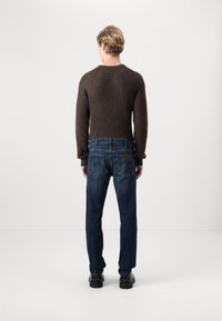 Bruine gebreide trui met geribbelde textuur, gecombineerd met donkerblauwe denim jeans met achterzakken en een leren label. Zwarte schoenen.