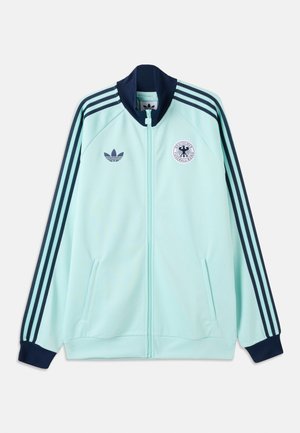 Jachetă sport de culoare albastru deschis cu guler și manșete bleumarin și trei dungi bleumarin pe mâneci, având logo-urile Adidas și Deutscher Fußball-Bund.