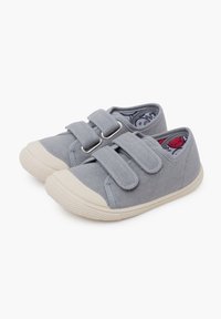 Chaussures en toile grises avec deux bandes velcro, embout en caoutchouc blanc et semelle en caoutchouc texturée. L'intérieur présente une doublure à motifs colorés.