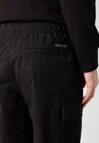 Čierne cargo nohavice Calvin Klein, s elastickým pásom, bočnými vreckami a malou značkovou etikettou na zadnej strane, vyrobené z odolného materiálu.