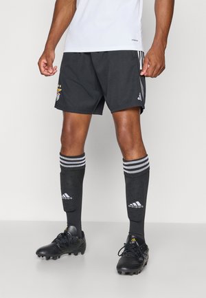 Sorte atletiske shorts med broderet logo, parret med knæhøje sorte sokker med grå striber, og sorte fodboldstøvler med struktureret overflade.